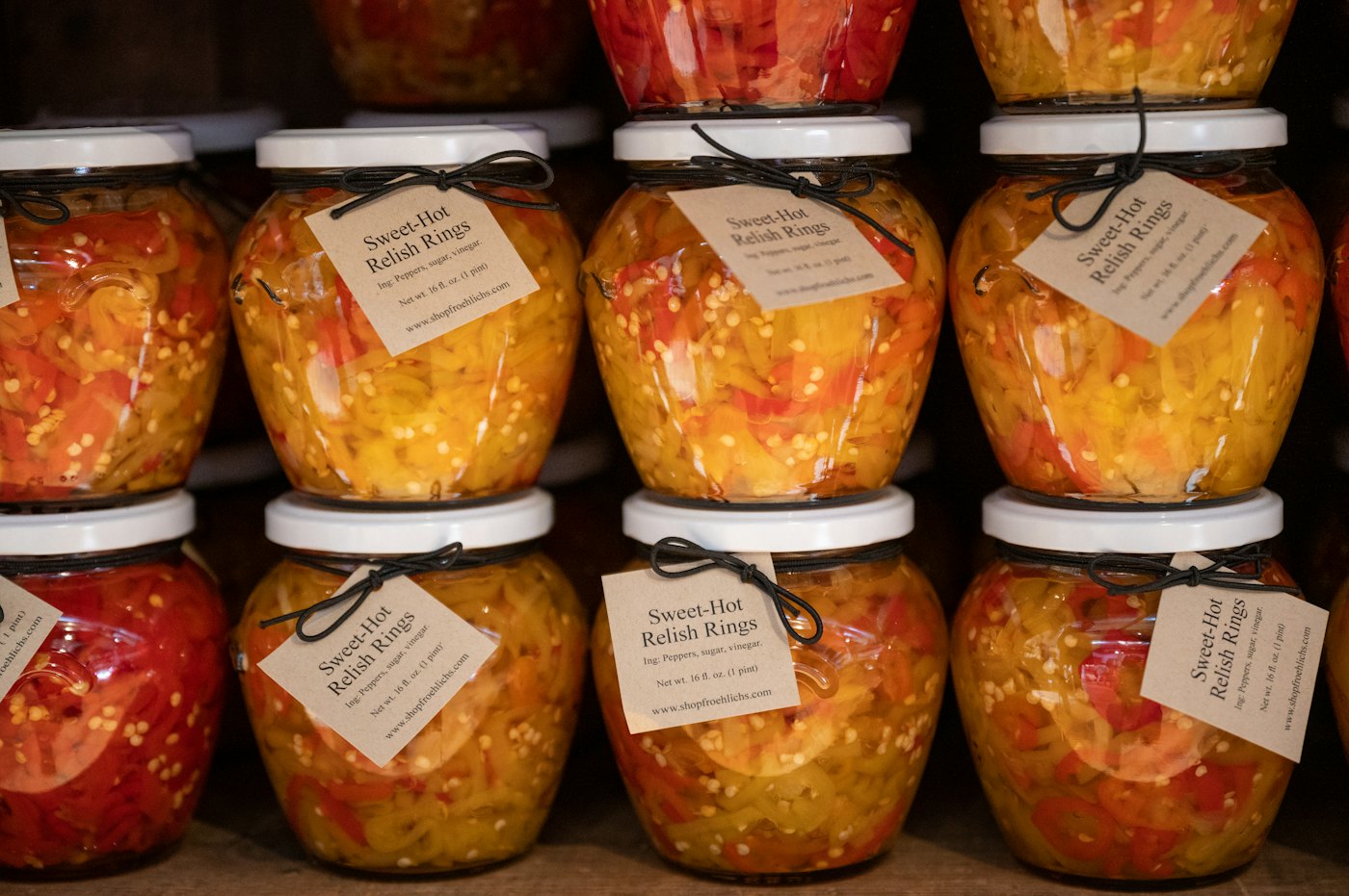Rows of glass jars filled with fermented vegetables on a wooden shelf.